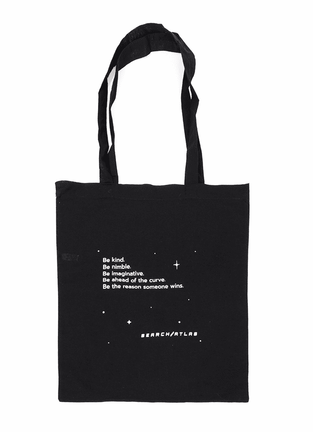 Black tote bag featuring inspirational message: "Be kind, be nimble, be imaginative, be ahead of the curve, be the reason someone wins" from Search Atlas store, perfect for daily use and promoting positivity.