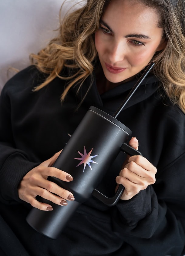 A sleek black tumbler with a colorful starburst design, perfect for hot and cold beverages, featuring a straw and handle for convenient use and portability.